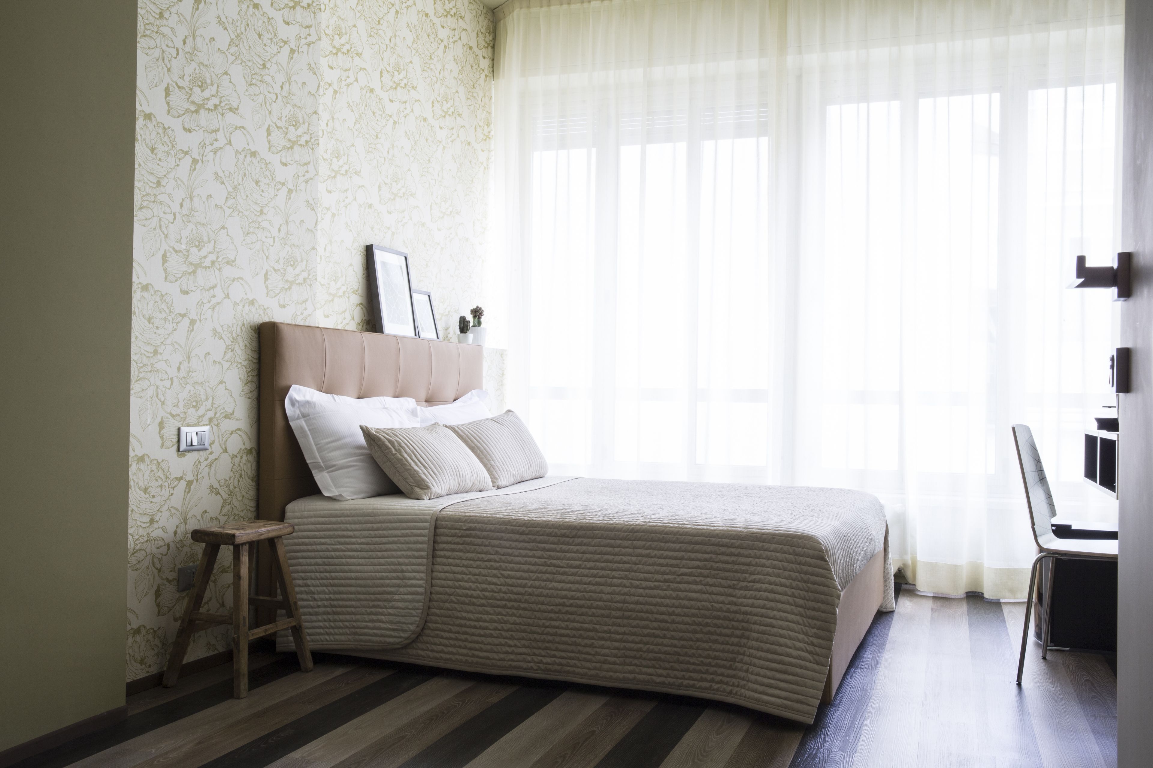 A neatly arranged bedroom with a bed, a small stool, and a chair.