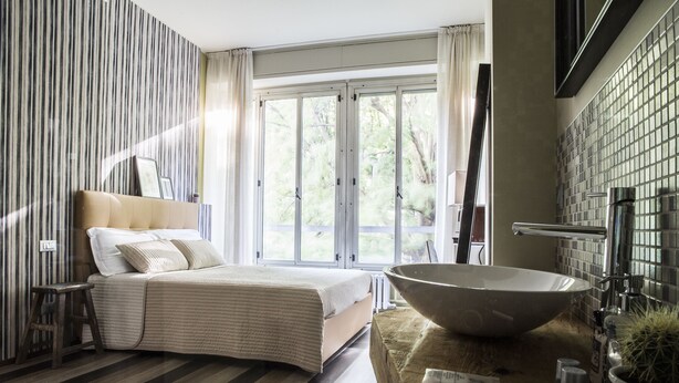 A bedroom with a large bed, a wooden stool, a large bowl sink, and a view of the outdoors. - Serendipity Rooms (Milan)