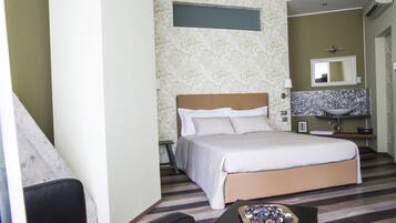 A hotel room with a bed, a small table, a chair, a bathroom with a sink and mirror, and a window.