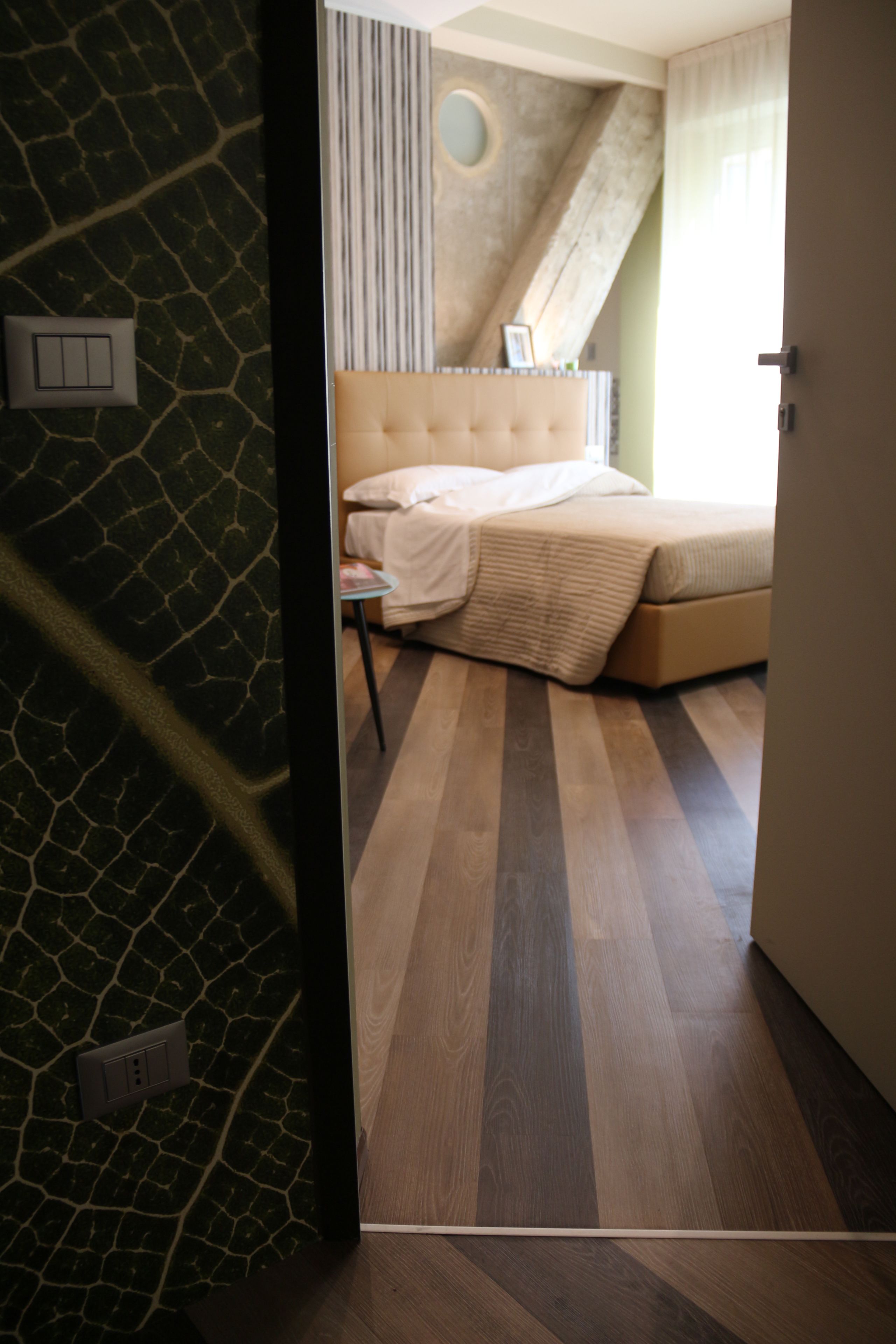 A bedroom with a bed, a nightstand, and a wall with a unique pattern.