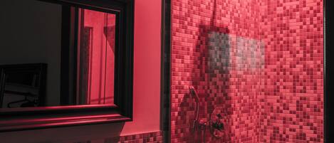 A bathroom with a red-tinted shower, a sink with a mirror, and a tiled wall.