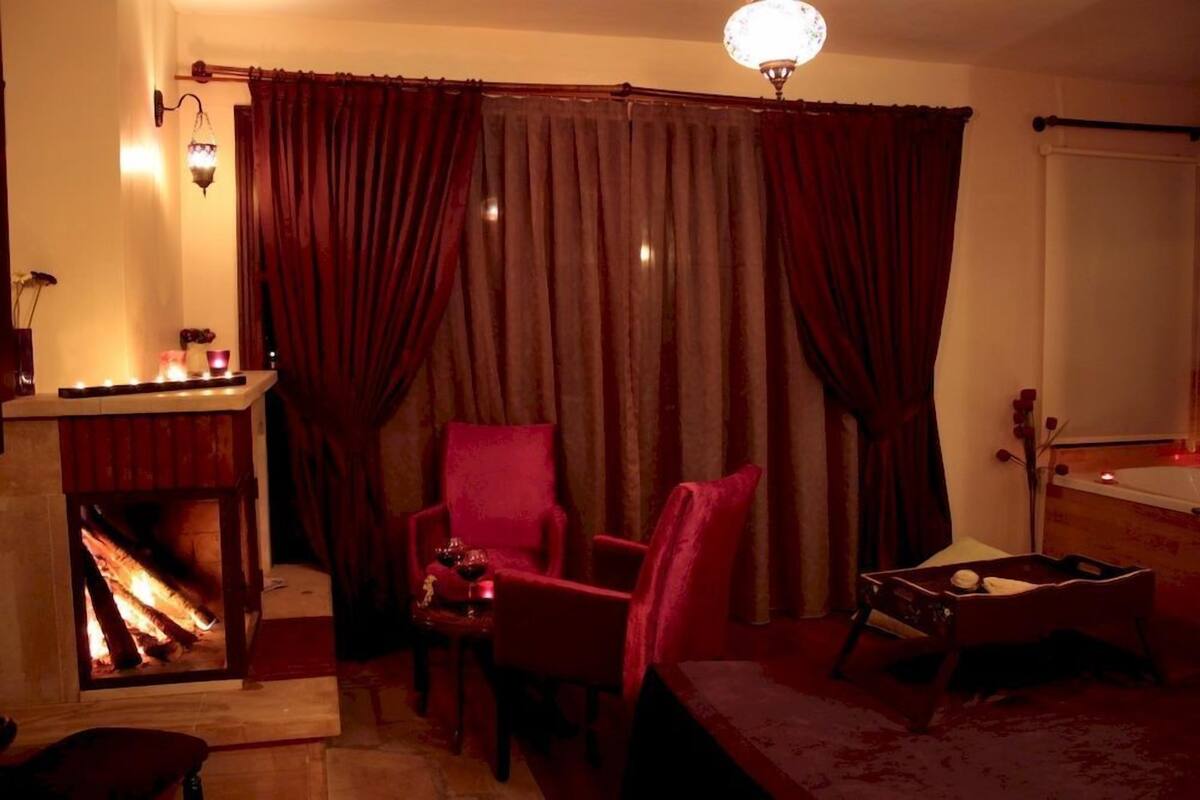 A cozy room with a fireplace, red chairs, and a small table with a candle.