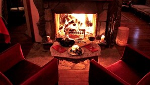 A cozy room with a stone fireplace, two red chairs, a table with candles, and a bottle of wine. - Villa Pine Garden (Sile)