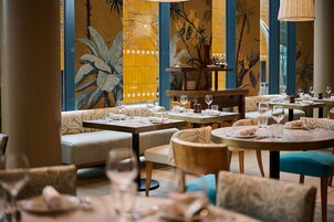 Un restaurante con mesas redondas y asientos acolchados, que presenta un mural tropical en las paredes.