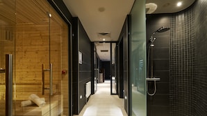 A modern bathroom with a glass shower enclosure, a wooden bench, and a tiled floor.