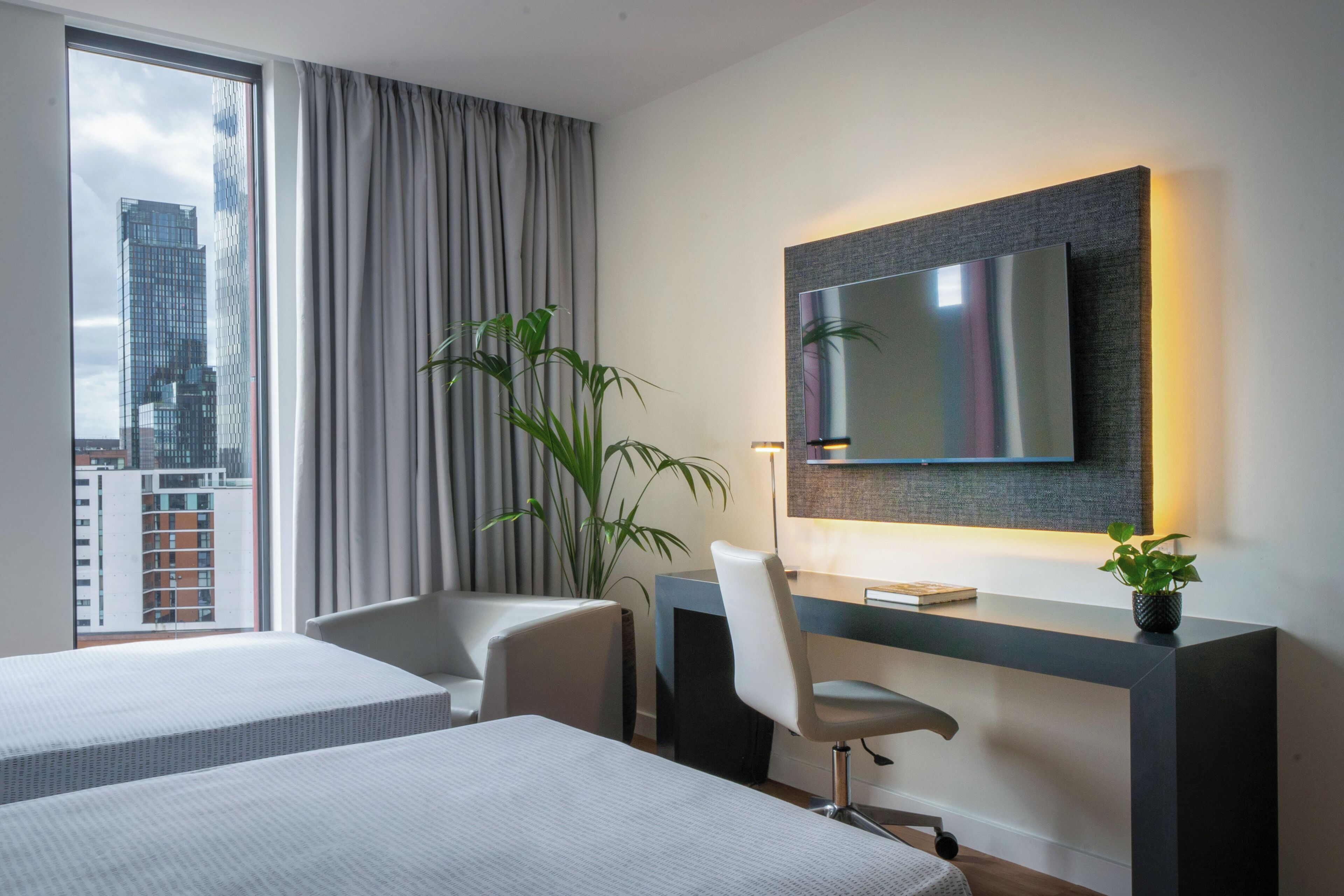 Une chambre d’hôtel dotée d’une grande fenêtre, d’un téléviseur à écran plat fixé au mur, d’un bureau avec une chaise et d’un lit.