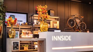 A reception area with a modern design, featuring a reception desk labeled "INNSIDE," a television displaying a mobile phone, and a bicycle leaning against the wall.