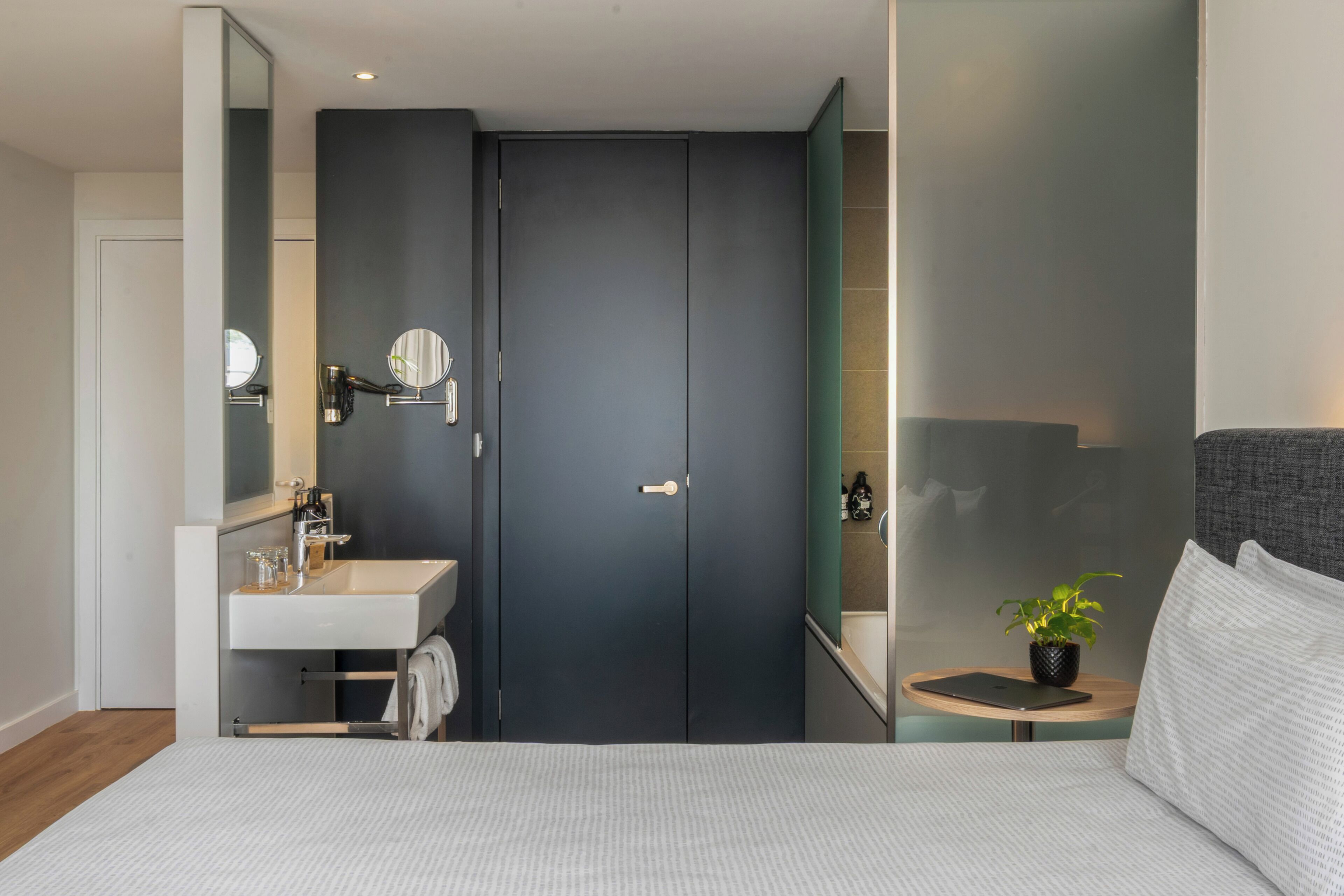 A modern bedroom with a bed, a bedside table with a lamp, a mirror, and a wardrobe.