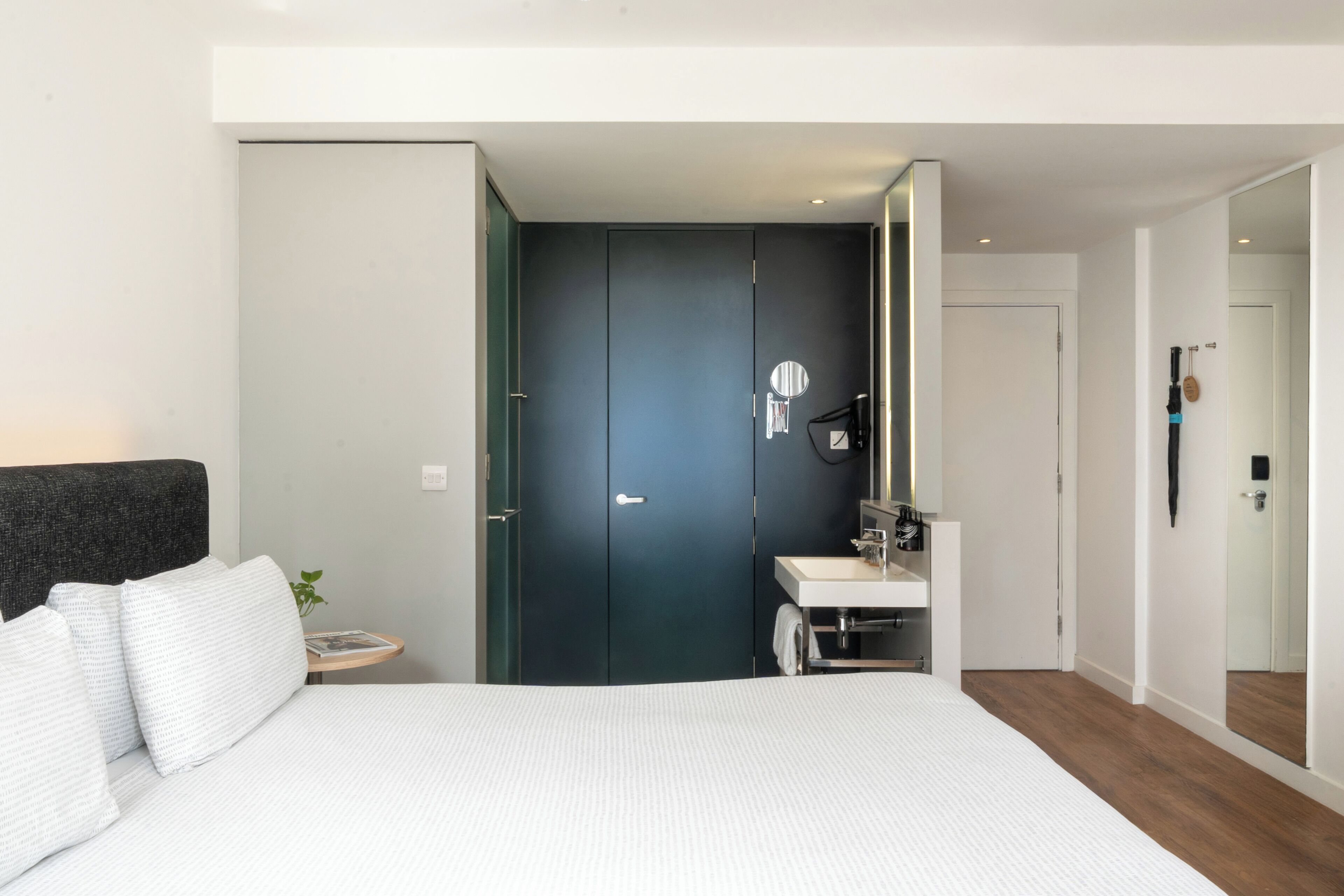 Een moderne slaapkamer met een bed, een nachtkastje, een spiegel en een donkere deur.