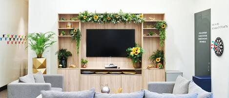 Un salon moderne avec un canapé gris, un téléviseur à écran plat, des étagères en bois et des plantes décoratives.