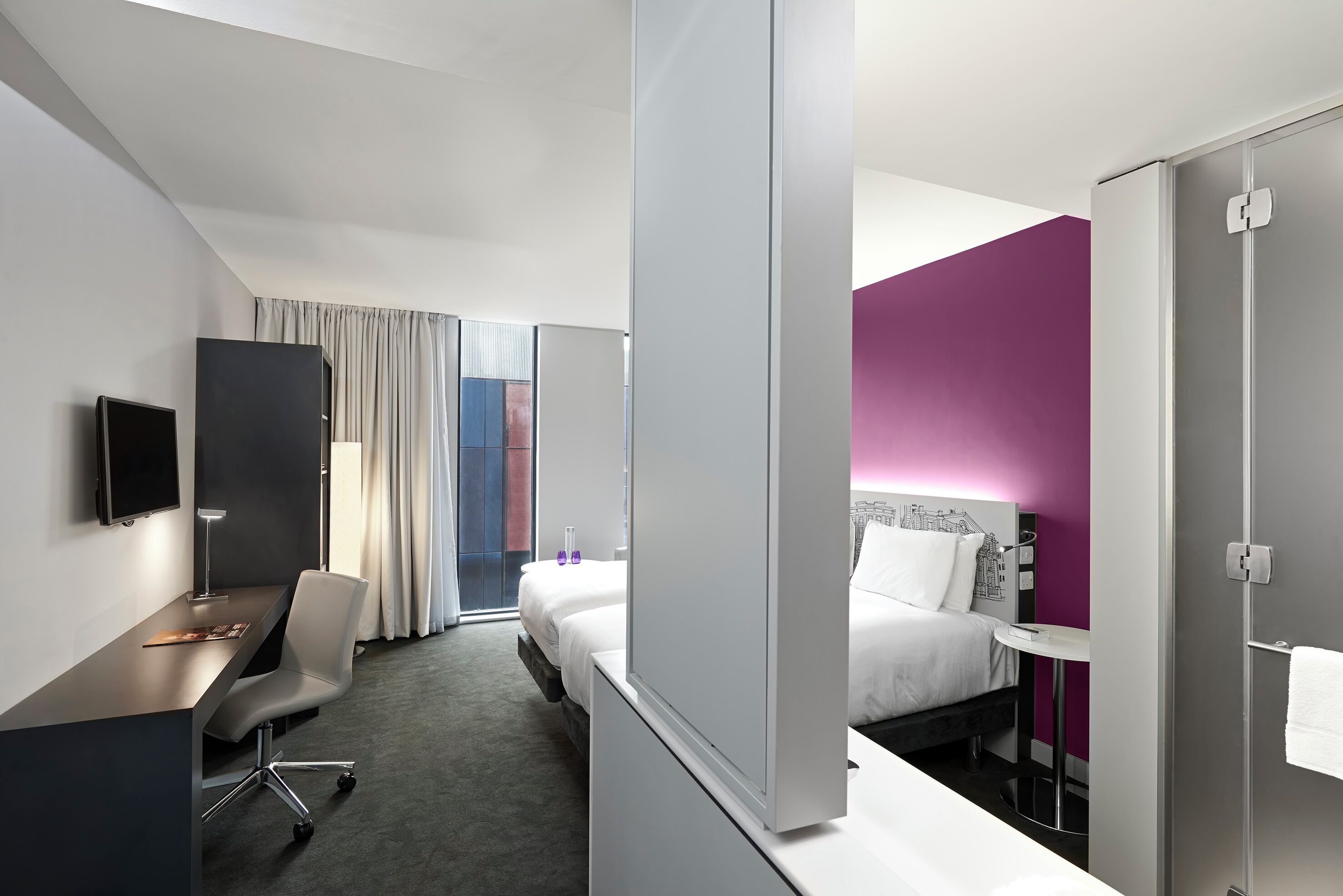 Une chambre d’hôtel moderne équipée d’un bureau, d’une chaise, d’un lit et d’une petite table.