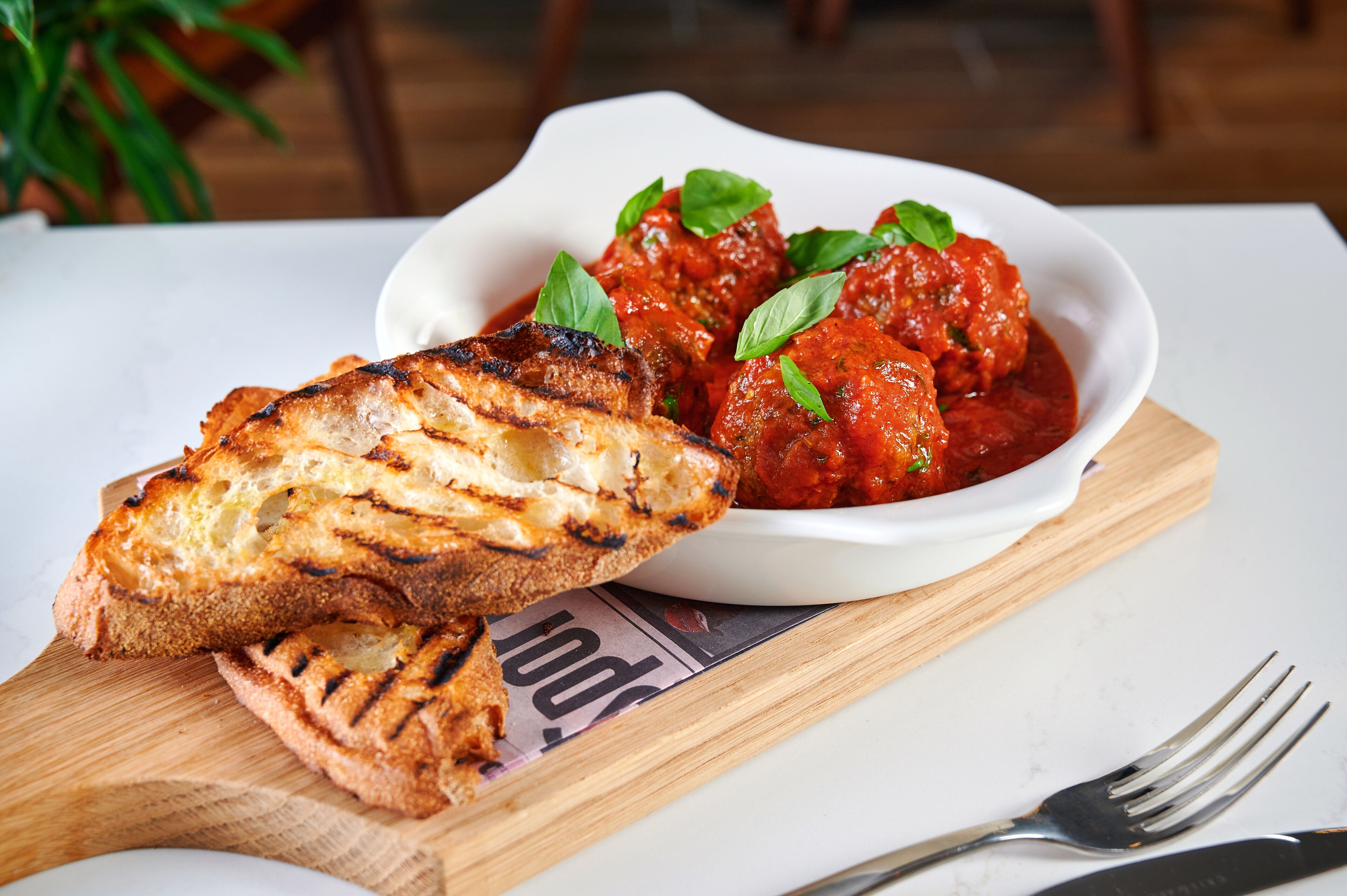 A plate of grilled bread and meatballs in tomato sauce on a wooden board.