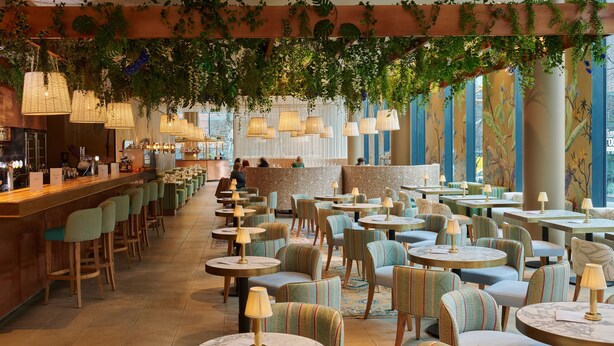 A restaurant with round tables and chairs, a bar area, and a view of the city through large windows.