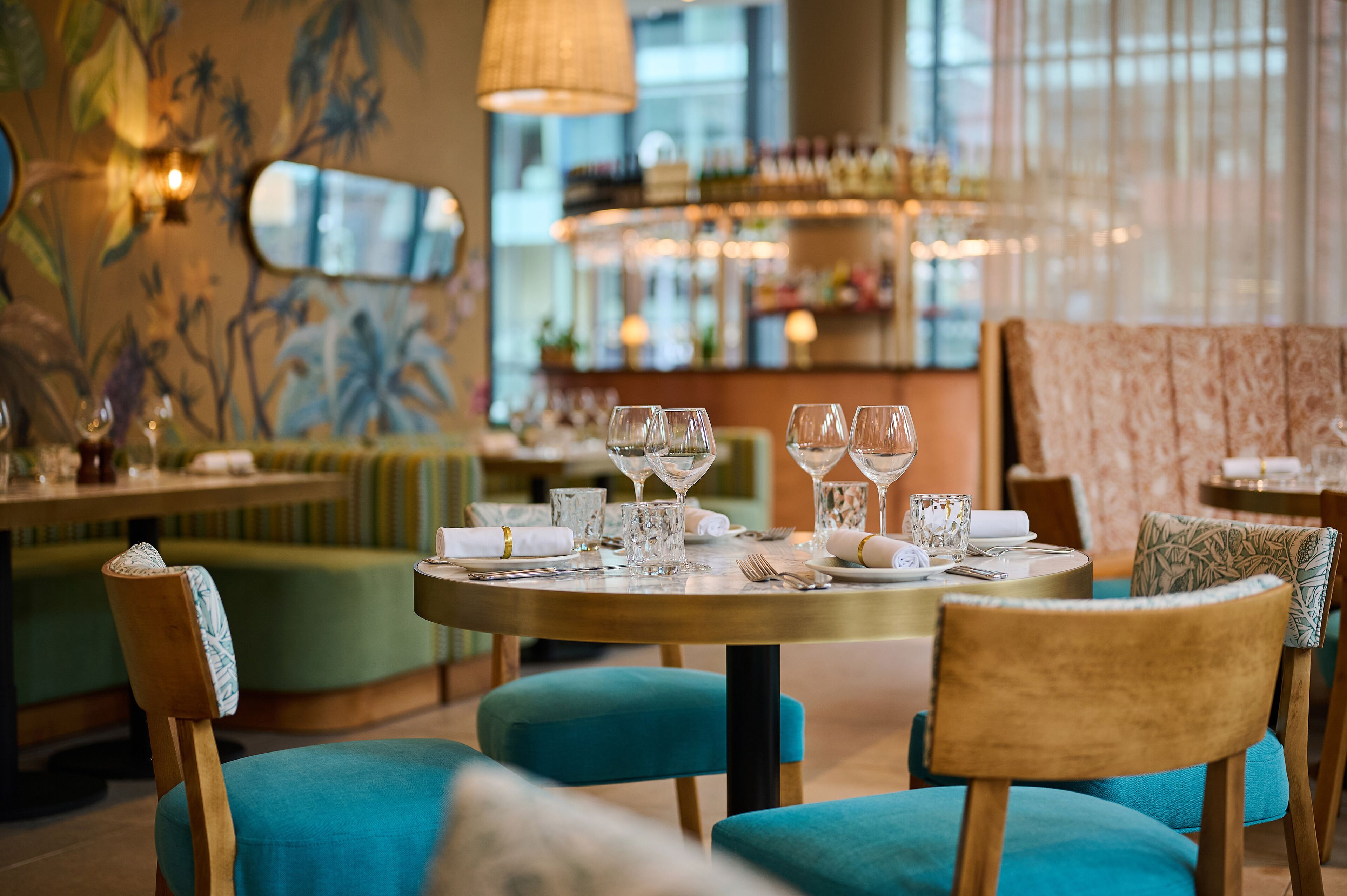 A restaurant interior with round tables, blue upholstered chairs, and a bar area in the background.