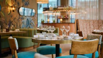 A restaurant interior with round tables, blue upholstered chairs, and a bar area in the background.