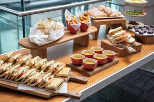 Una mesa de buffet con sándwiches, pasteles y tazas de café.
