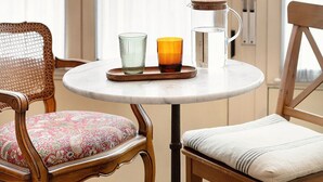 A round table with a pitcher, two glasses, and a tray in a room with large windows and wooden chairs. - Okako Hotel (San Sebastián)