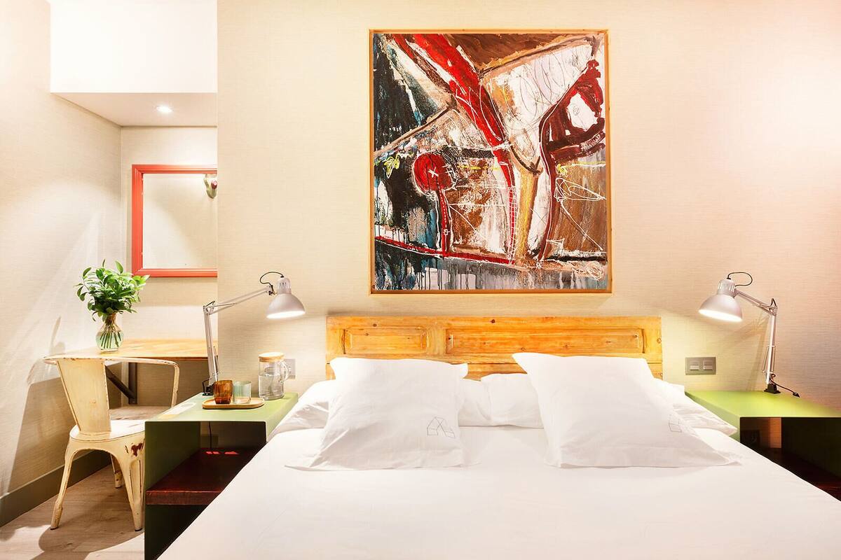 A hotel room with a large bed, two bedside tables with lamps, a desk with a chair, and a large abstract painting on the wall.