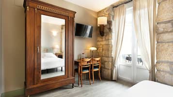 Habitación de hotel con un amplio armario de madera, un escritorio con dos sillas, un televisor montado en la pared y una pared de piedra.