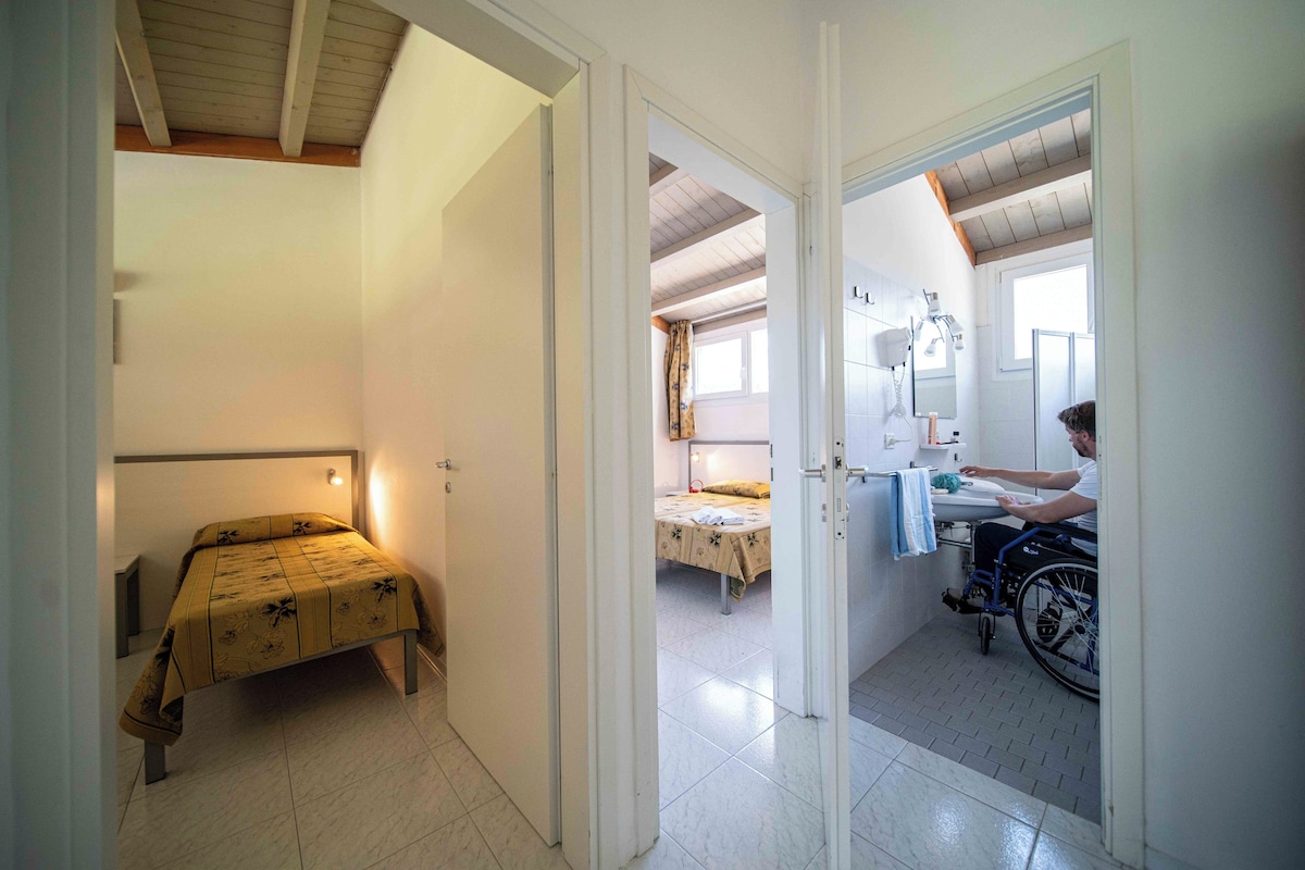 Una habitación con cama, silla de ruedas y baño con espejo y lavabo.