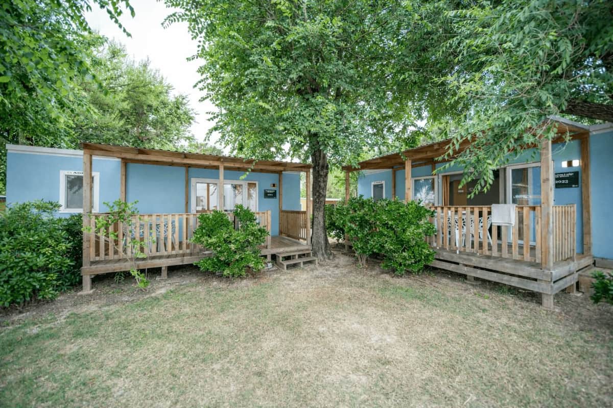 Deux petites cabanes dotées de terrasses en bois, entourées d’arbres et d’herbe.