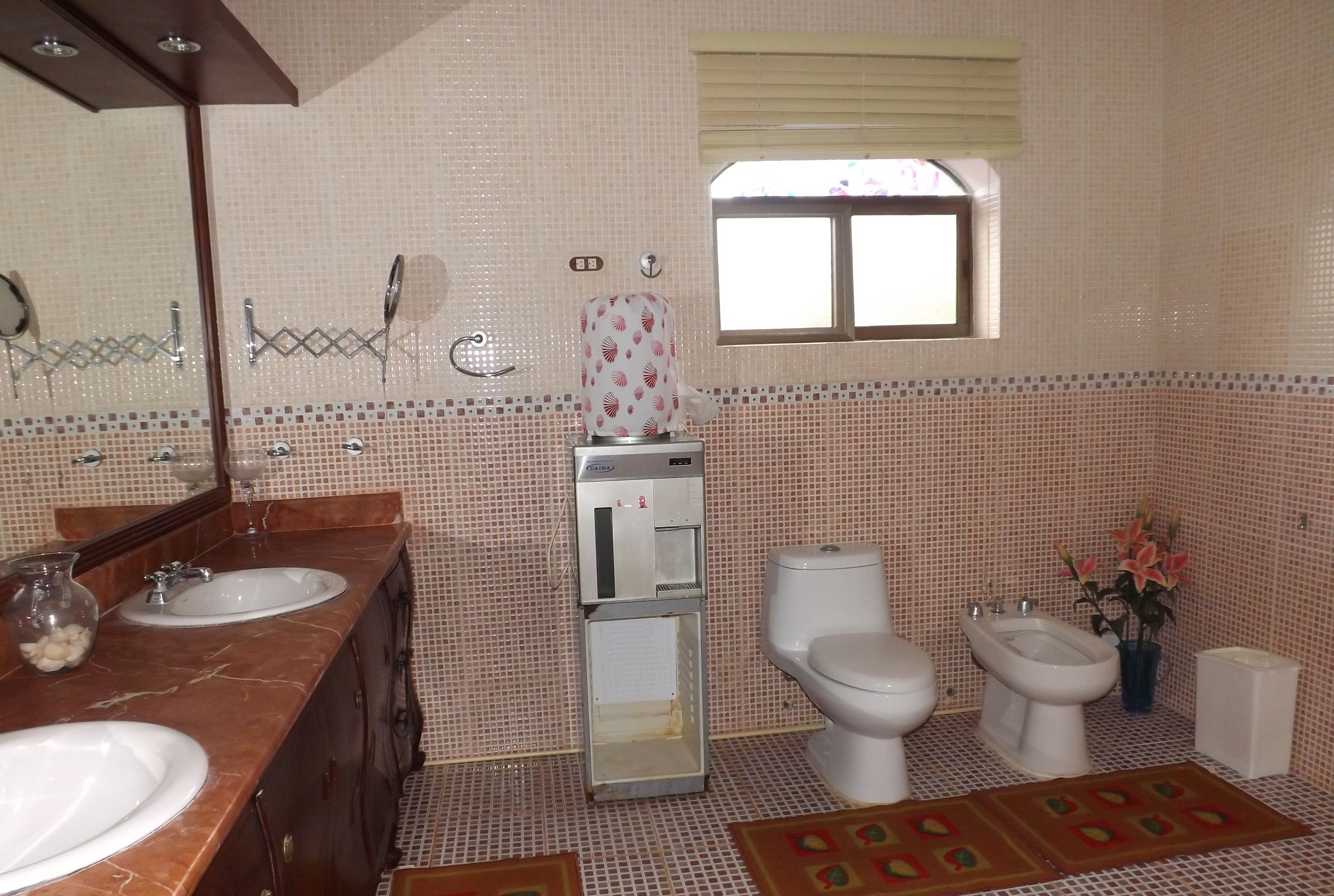 Une salle de bain avec deux lavabos, des toilettes, un bidet, un miroir et une fenêtre.