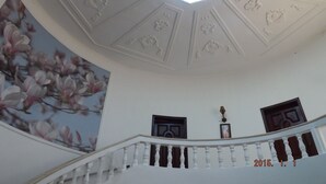 Eine Treppe mit weißer Balustrade, eine Decke mit floralen Mustern und ein großes Blumenbild an der Wand.