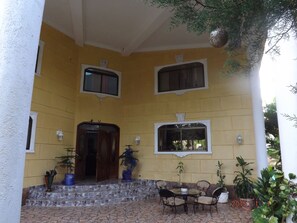 A yellow building with a tiled entrance, potted plants, and a seating area with chairs and a table. - Four Bedroom Villa with Private Pool, Ocean View (Sosúa)