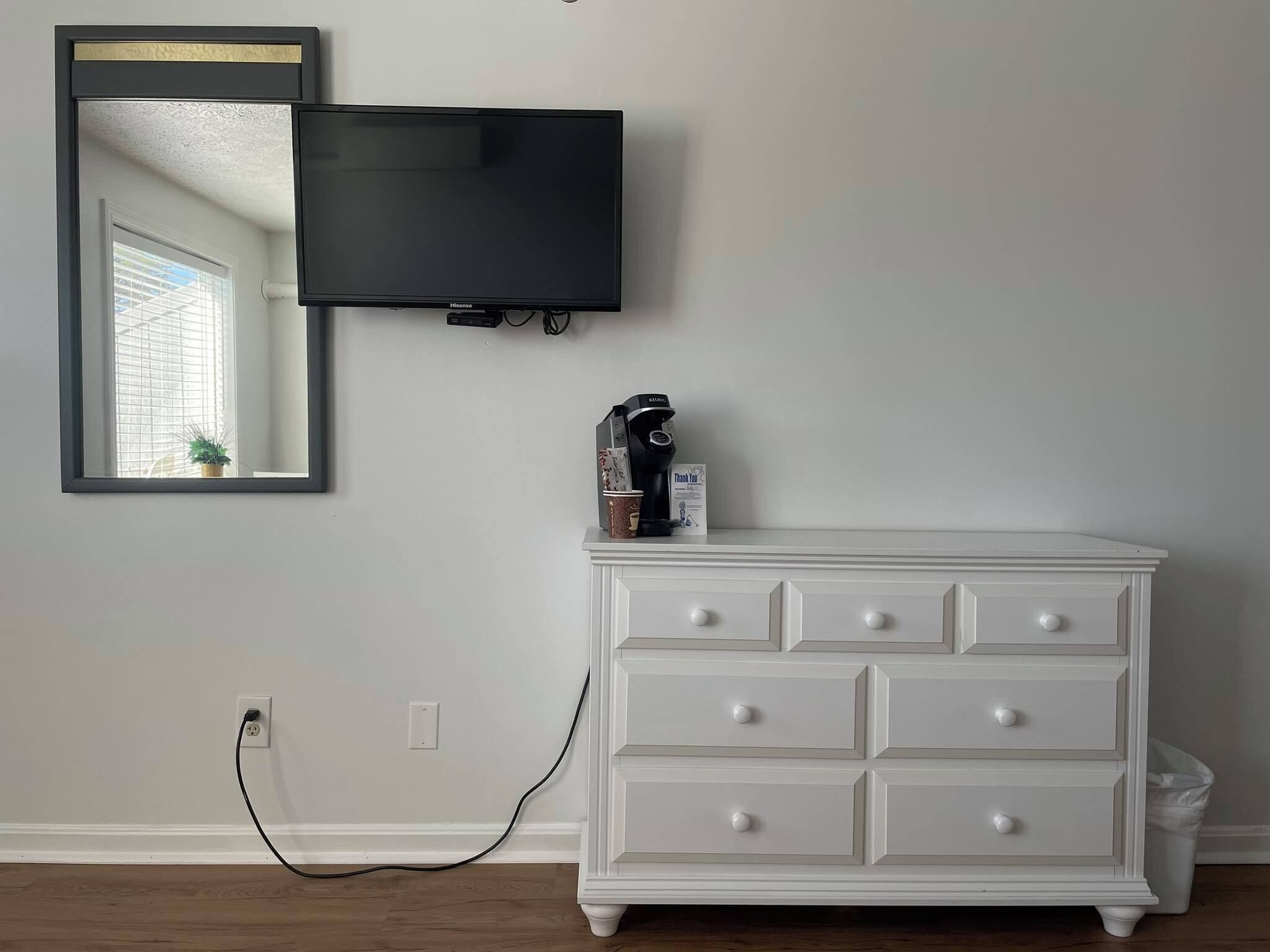 A room with a white dresser, a flat-screen TV mounted on the wall, and a mirror above the dresser.