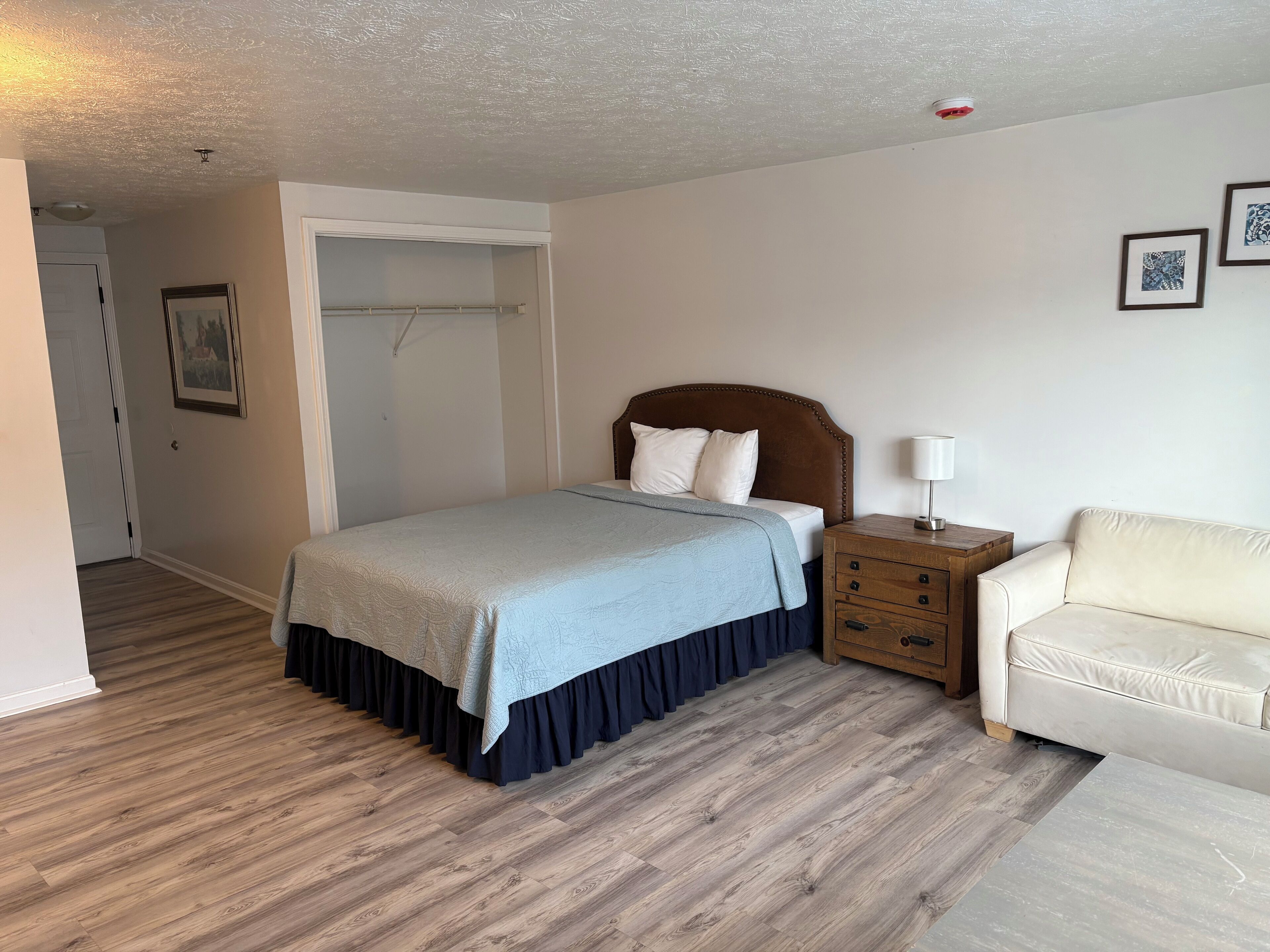 A bedroom with a bed, a nightstand, a chair, a wardrobe, and a door.