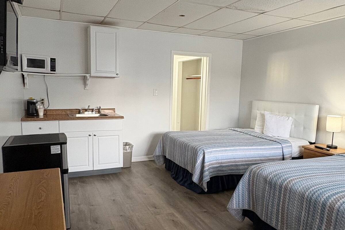 A hotel room with two beds, a kitchenette, a microwave, a coffee maker, and a trash can.