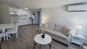 A modern living room with a sofa, a round coffee table, and a dining area with chairs and a table. - Grand Beach Inn (Old Orchard Beach)