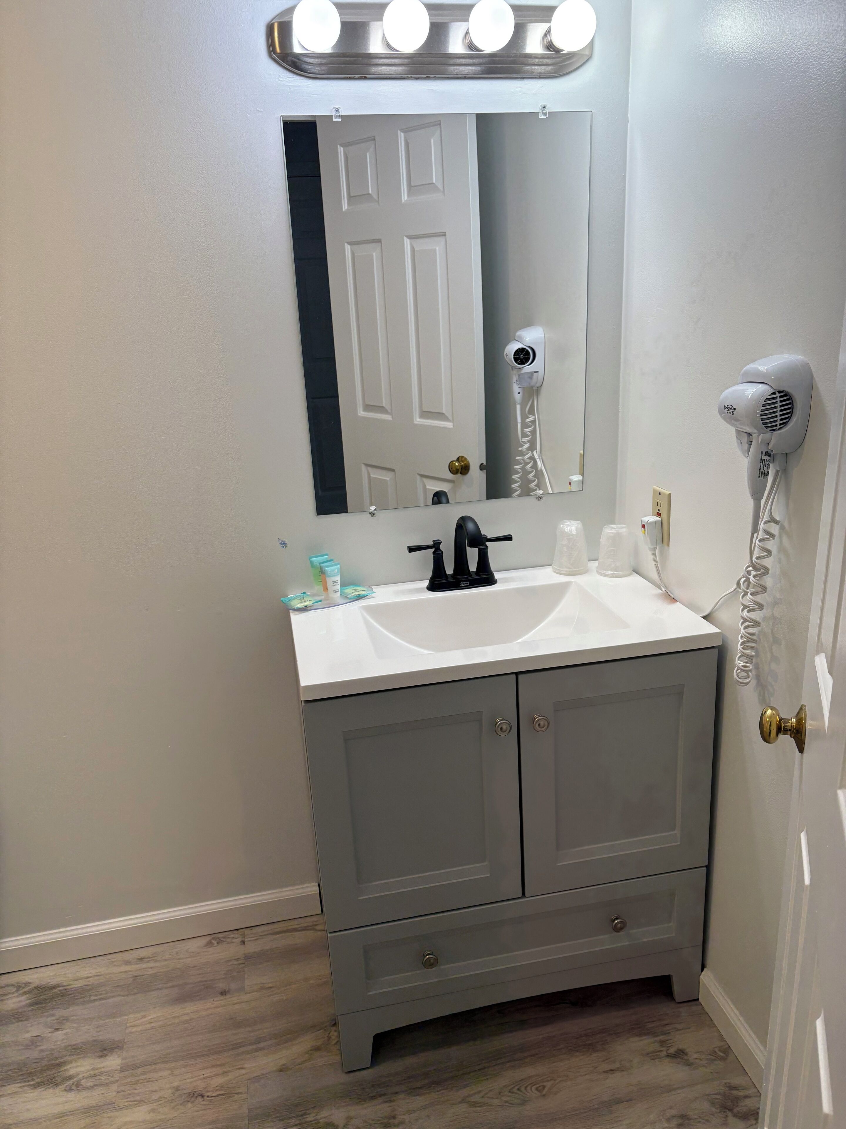 A bathroom with a white sink, a mirror, a hair dryer, and a door with a brass doorknob.