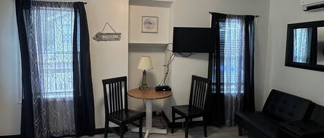 A living room with a black sofa, a small round table with two chairs, a lamp, and a framed picture on the wall.