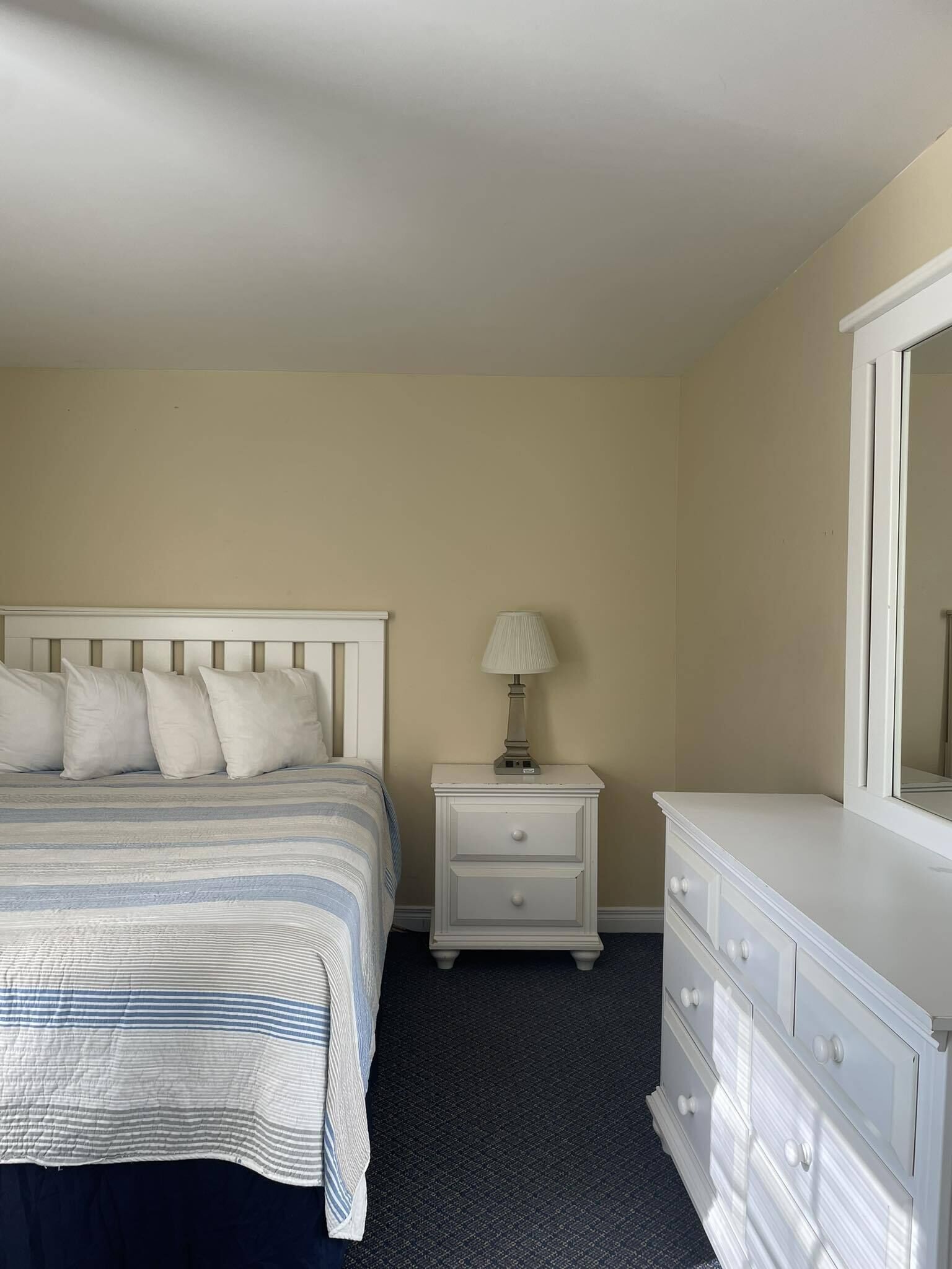 A bedroom with a bed, nightstand, dresser, and mirror.