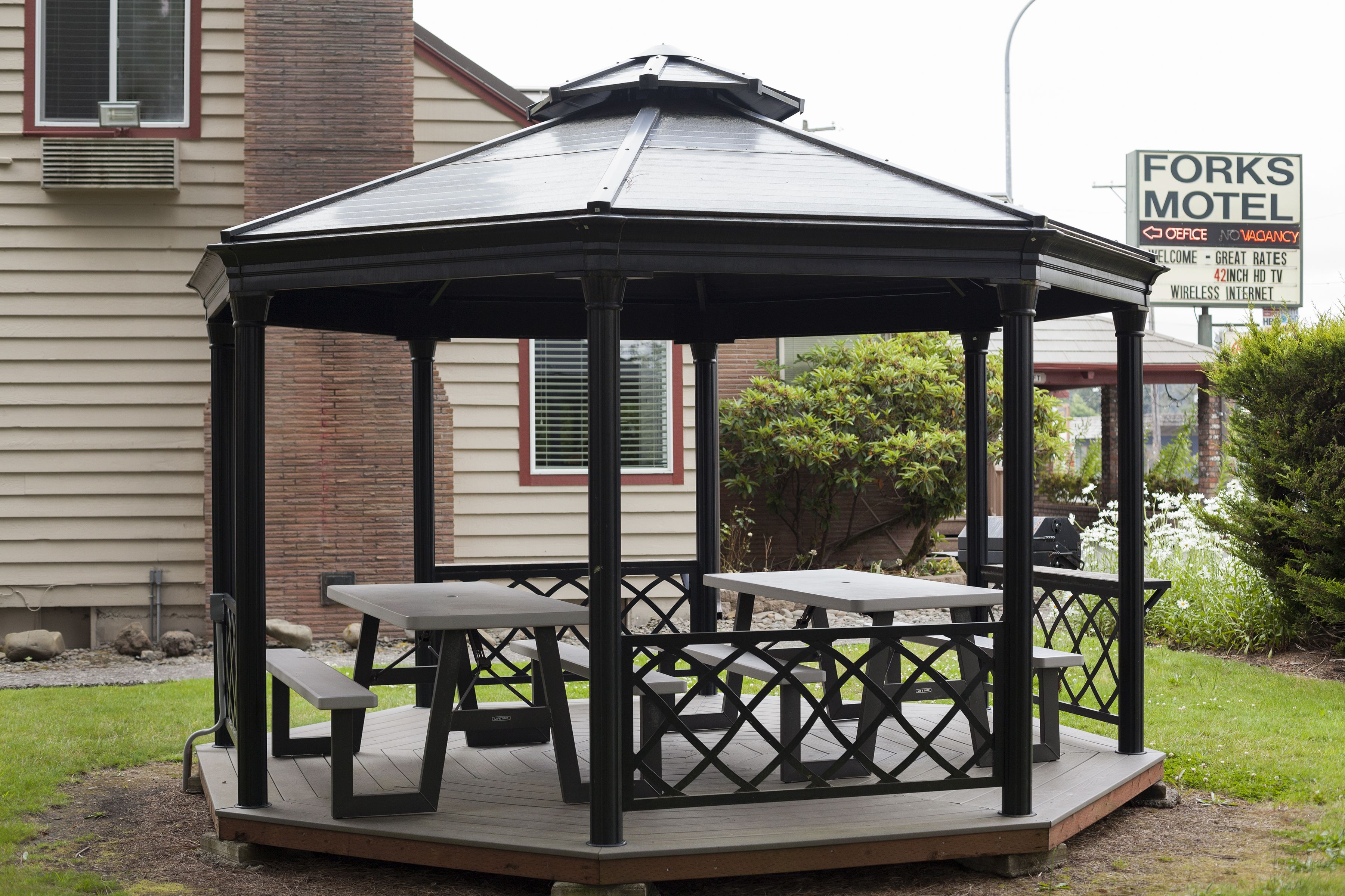 A gazebo with picnic tables and benches, surrounded by a brick wall and greenery.