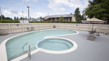 A swimming pool with a small hot tub, surrounded by a wooden fence, with a house and trees in the background.