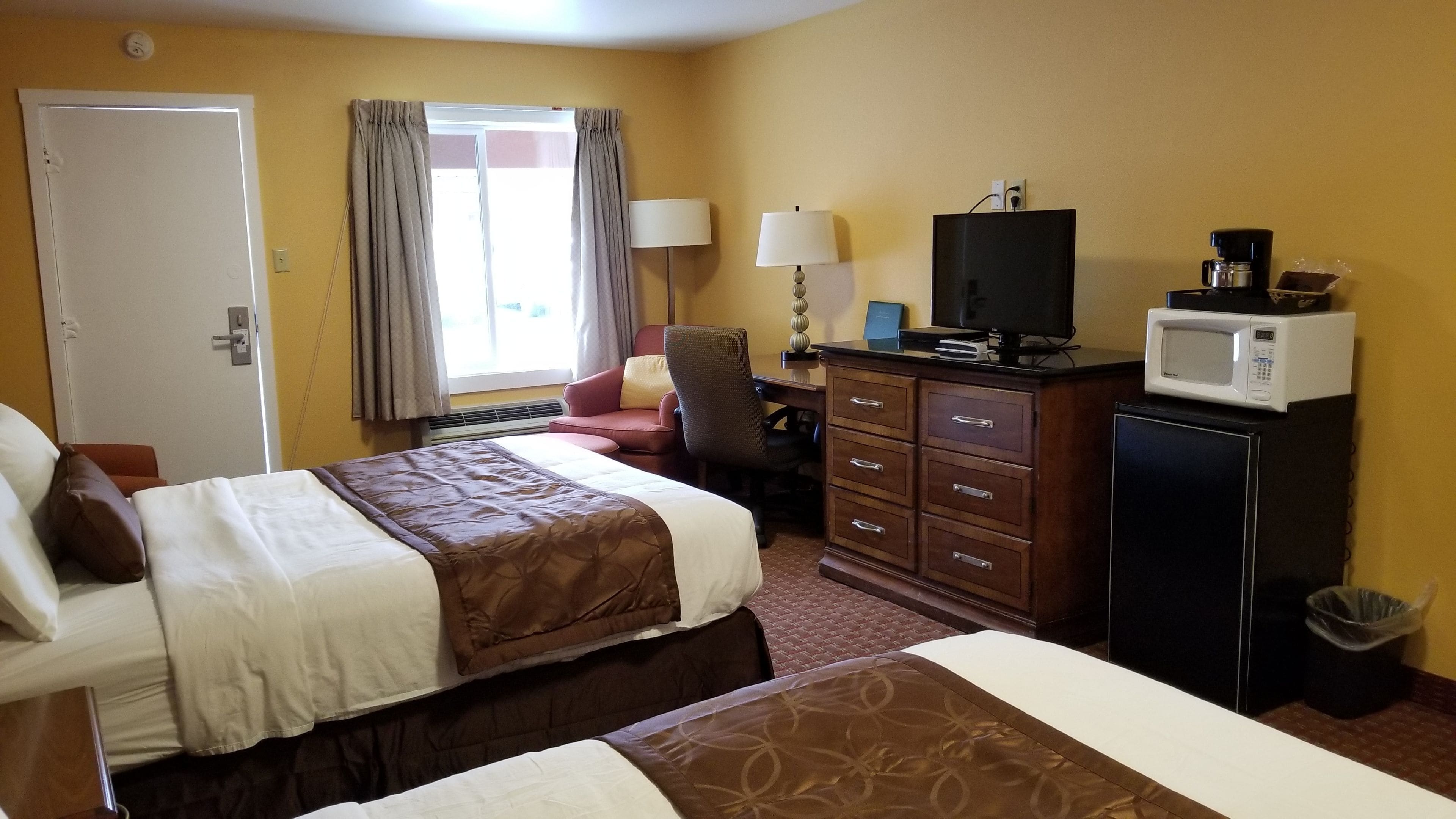A hotel room with two beds, a desk with a computer, a television, a microwave, and a trash can.
