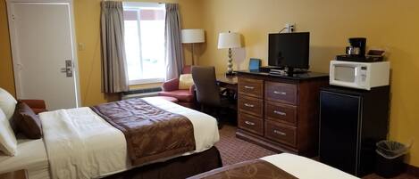 A hotel room with two beds, a desk with a computer, a television, a microwave, and a trash can.