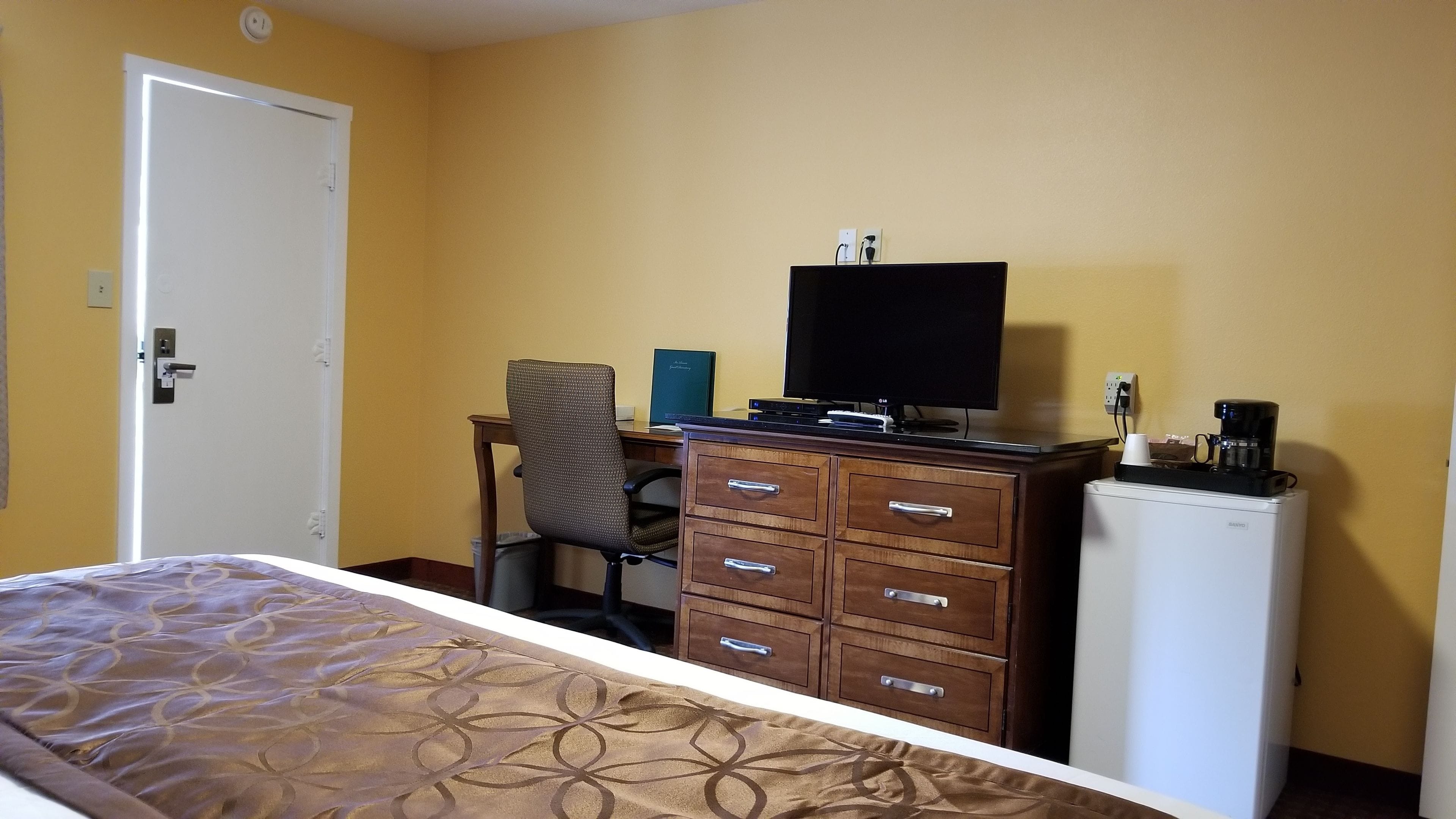 Een hotelkamer met een bed, een bureau met computer, een stoel, een kledingkast en een koelkast.