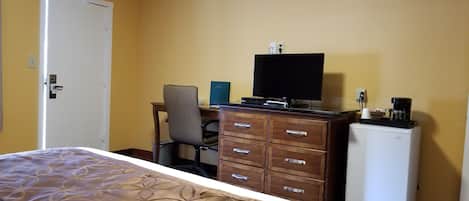 Een hotelkamer met een bed, een bureau met computer, een stoel, een kledingkast en een koelkast.