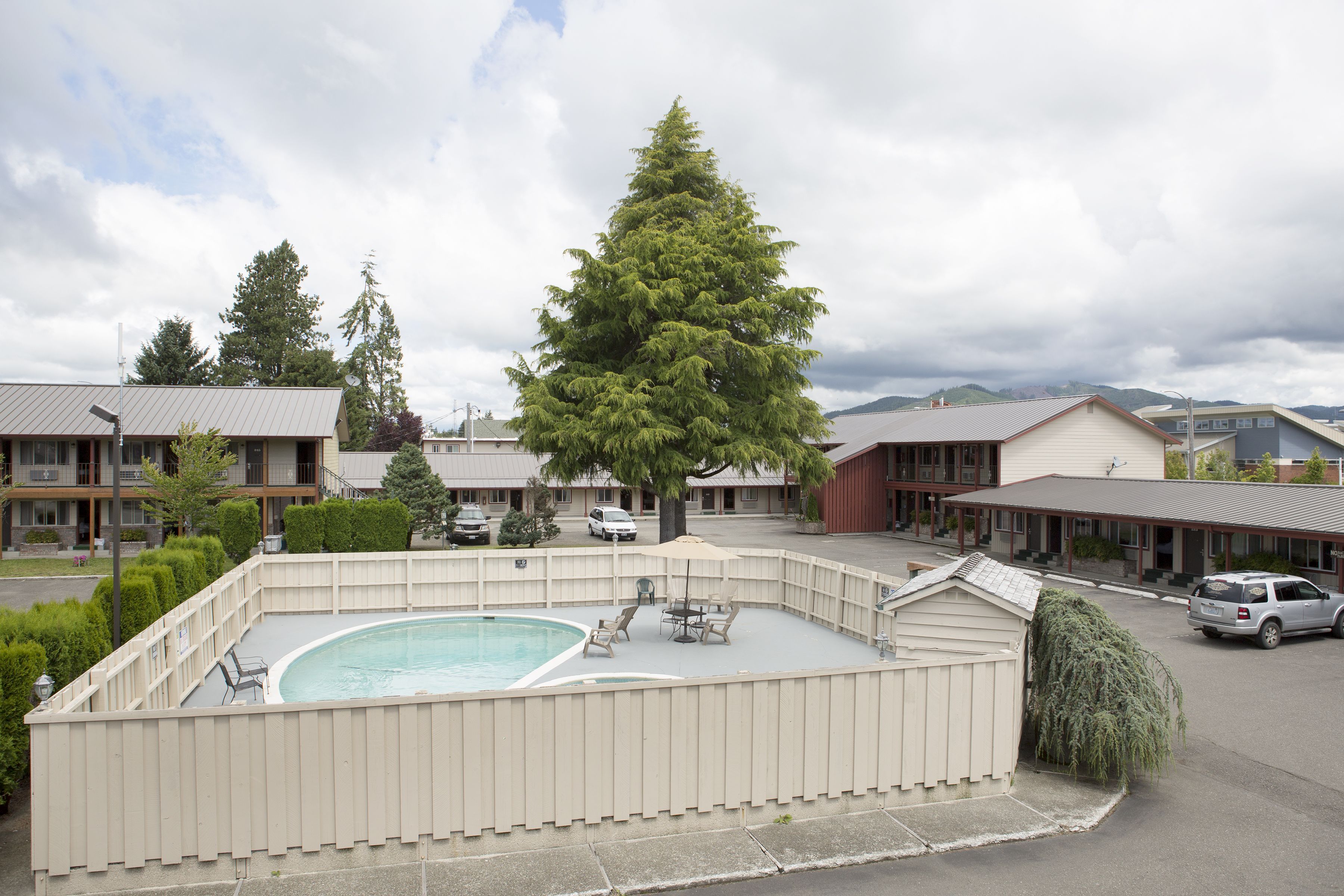A swimming pool with lounge chairs and a small shed, surrounded by a fence, with buildings and trees in the background.