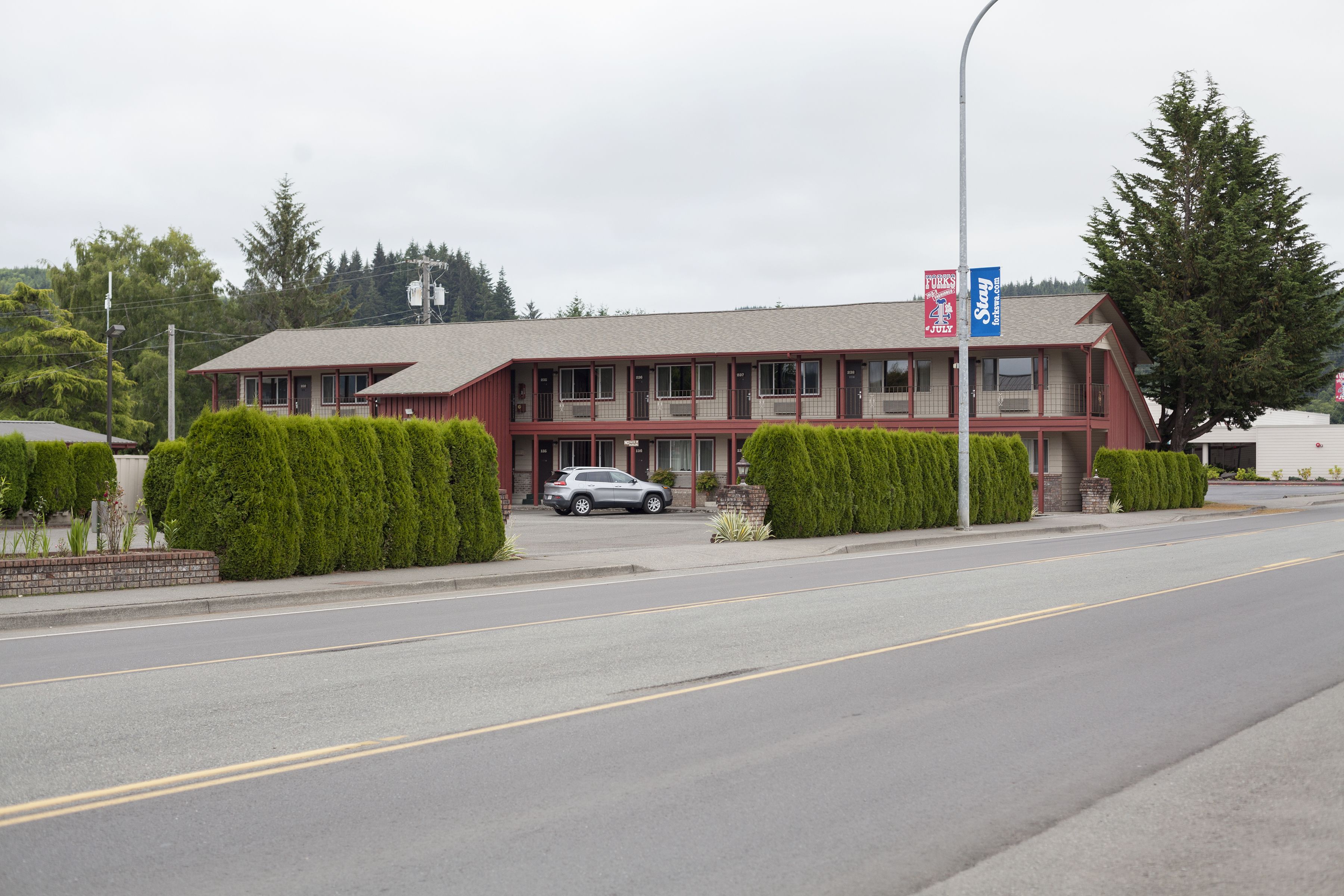 Un motel à deux étages avec une façade rouge, une voiture garée devant et une enseigne bleue sur la droite.