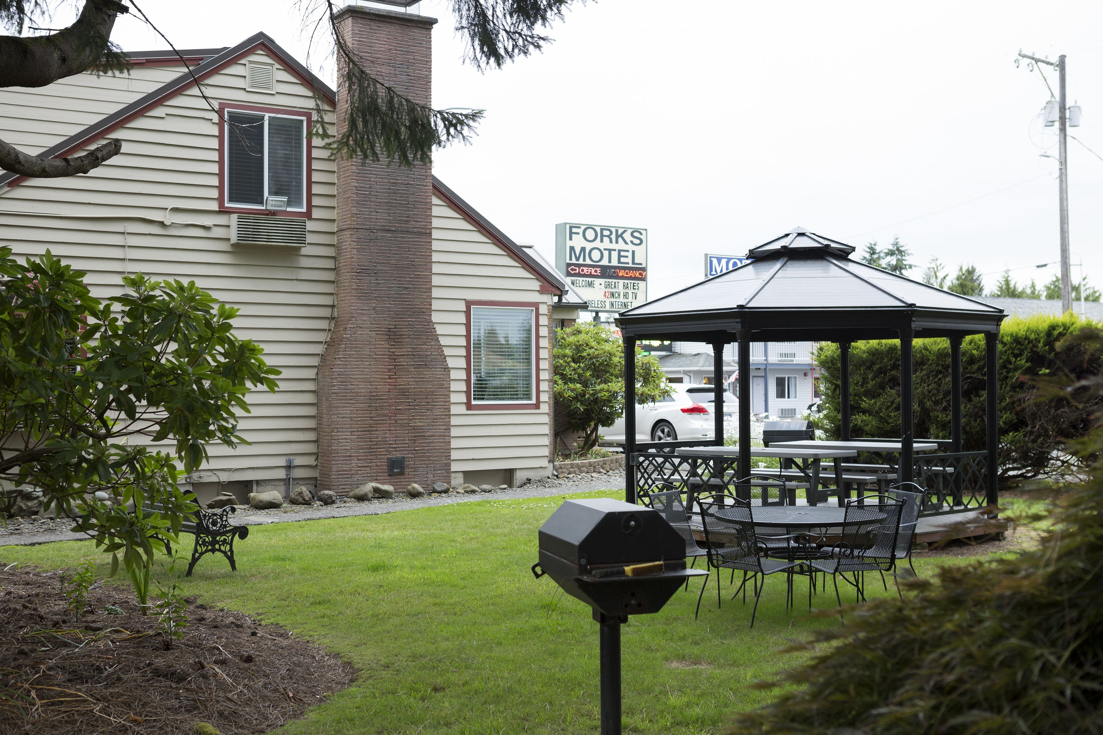 A gazebo with a table and chairs, a barbecue grill, and a motel sign in the background.