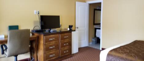 A hotel room with a wooden desk, a chair, a television, a dresser, and a bed.
