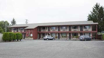A multi-story motel with a flat roof, two cars parked in front, and a clear sky.
