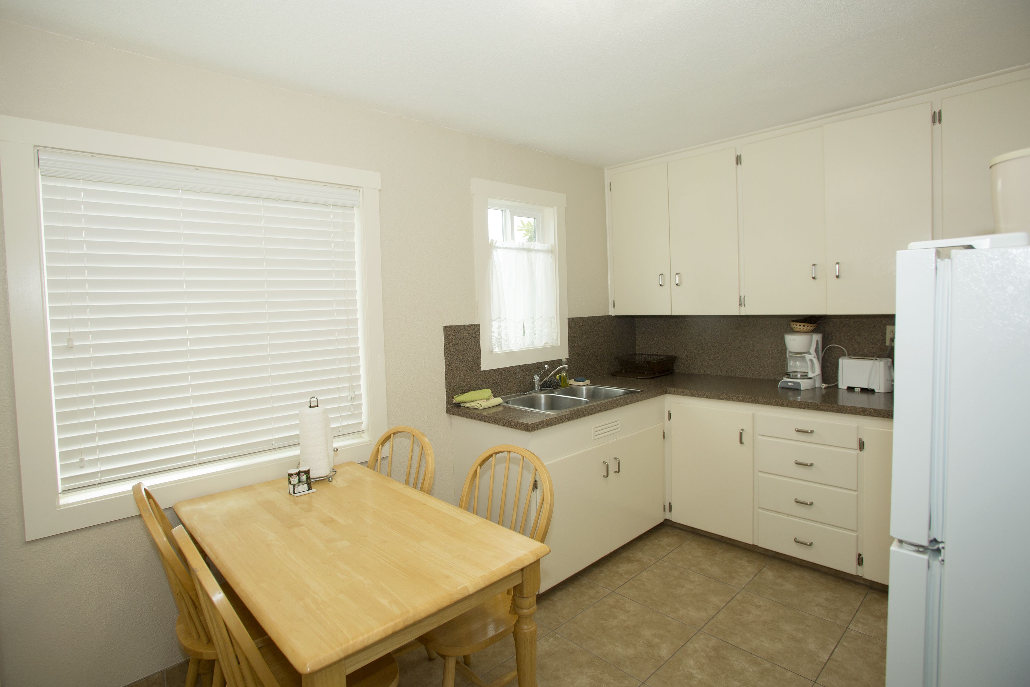 Una cocina con una mesa de madera, sillas, un lavamanos, armarios y un refrigerador.