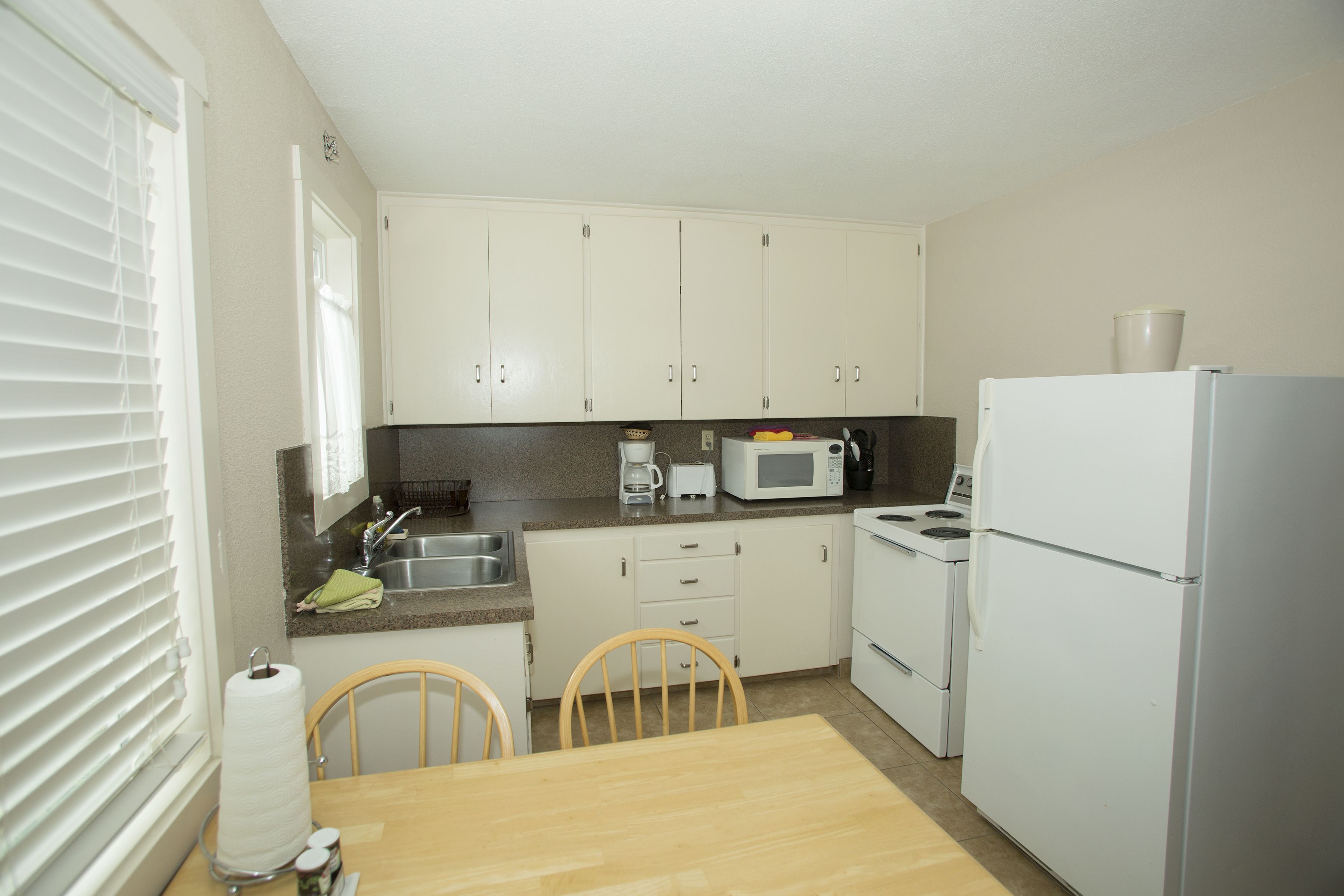 A compact kitchen with white cabinets, a microwave, a stove, and a refrigerator.