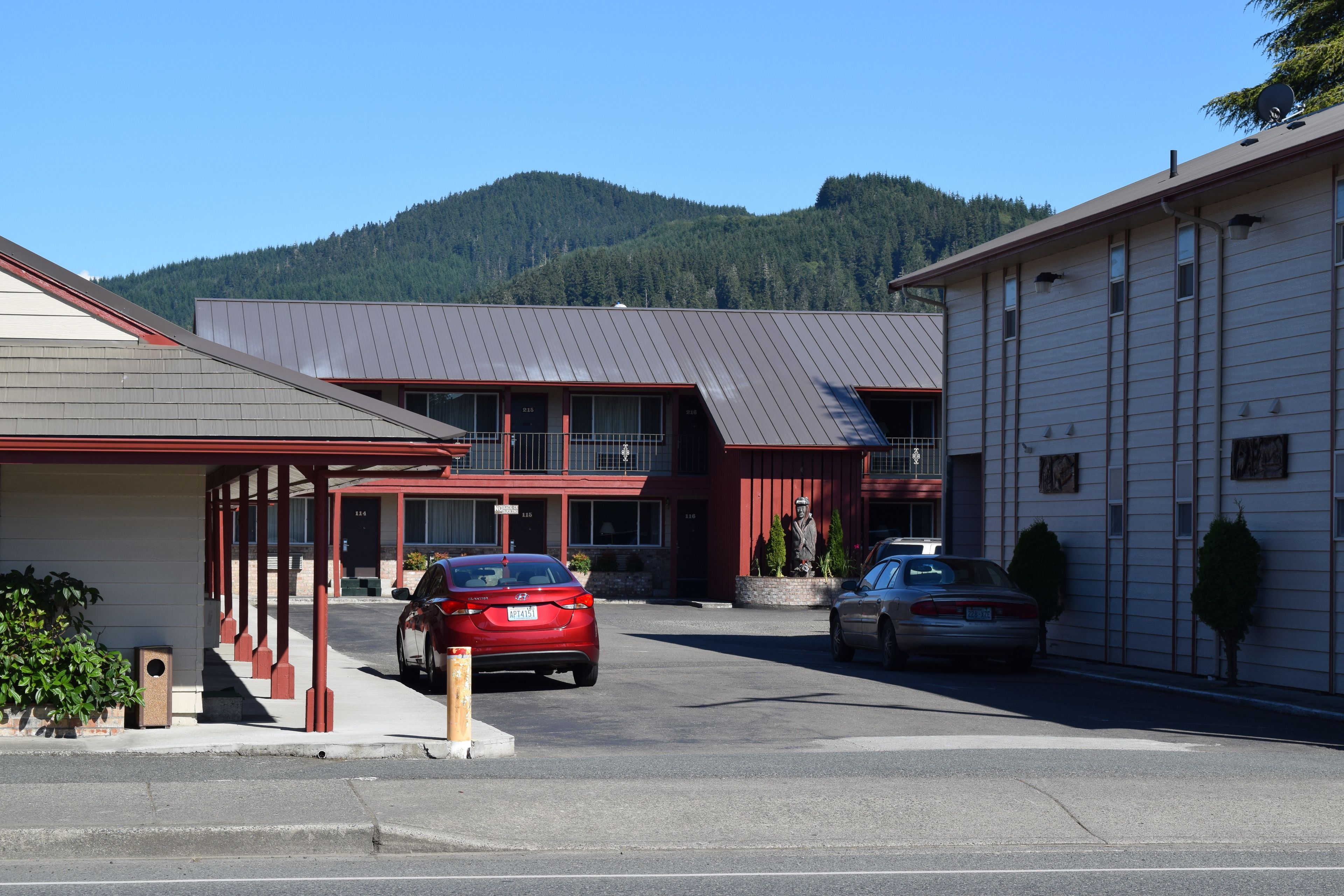 Un bâtiment à la façade rouge et blanche, doté d’un espace de stationnement couvert et surplombant un paysage montagneux.