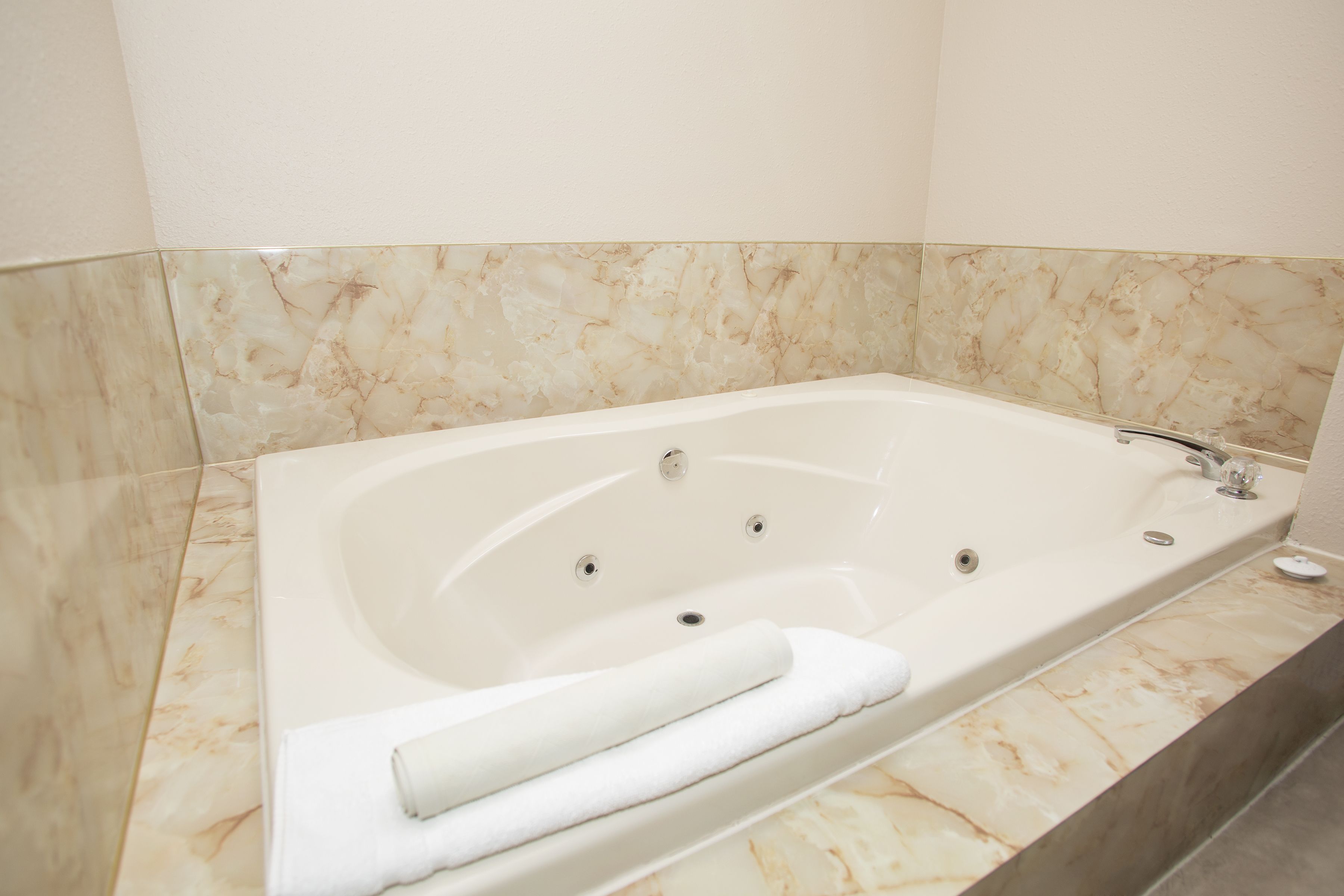 Una bañera grande y rectangular con un solo grifo y un asiento integrado, frente a una pared con azulejos de mármol.